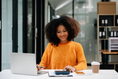 Çekici, gülümseyen Afrikalı kadın defter, tablet ve dizüstü bilgisayarla yazmayı düşünerek evden kameraya bakıyor.