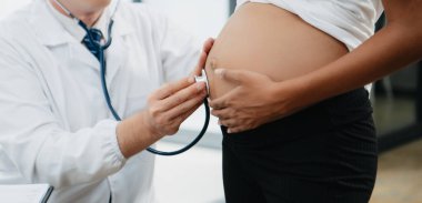 Hamile Afrikalı kadının klinikteki doktorla randevusu var. Stetoskop kullanan jinekolog erkek jinekolog kadın doğum uzmanı annesinin karnındaki bebeğin kalp atışlarını dinliyor. Hamilelik, sağlık konsepti