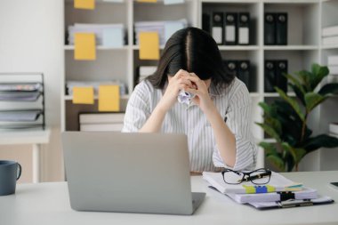 Woman who is tired and overthinking from working with tablet and laptop at office.