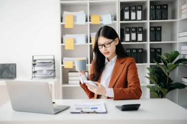 Ofiste elinde not defteri ve tabletle gülümseyen kendine güvenen Asyalı kadın.