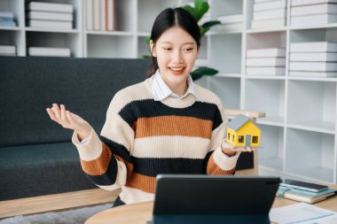 Ev modeli emlakçı ve müşteriyle birlikte çalışan Asyalı bir kadın ev, sigorta veya kredi emlak danışmanlığı için ev kredisi teklifiyle ilgili sözleşme üzerinde tartışıyorlar.