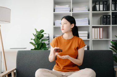  Kadın depresyonda oturur koyu renk saçlı dalgın bakışlar elinde bir bardak su ve haplarla pencerede durur.. 