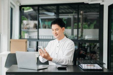 Masada oturan Asyalı bir adam dizüstü bilgisayar kullanarak ofiste Finans ve Pazarlama ile uğraşıyor.