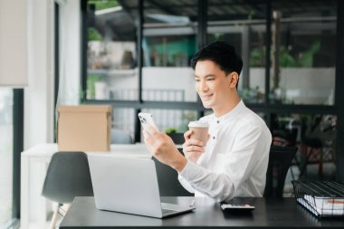 Masada oturan Asyalı bir adam dizüstü bilgisayar kullanarak ofiste Finans ve Pazarlama ile uğraşıyor.