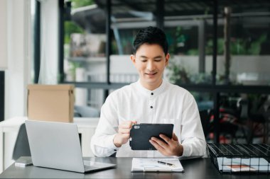 Tablet ve dizüstü bilgisayarda yazan yakışıklı genç adam ahşap masa modern ofisinde otururken.