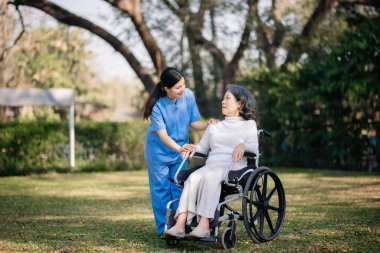 Asyalı genç bakıcı hemşire yaşlı bir erkeğin dışarıda yürümesini destekliyor. Uzman doktorlar yaşlı yetişkinlere yardım eder ve onlarla ilgilenir. Huzurevi hastane bahçesi konsepti