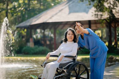 Asyalı genç bakıcı hemşire yaşlı bir erkeğin dışarıda yürümesini destekliyor. Uzman doktorlar yaşlı yetişkinlere yardım eder ve onlarla ilgilenir. Huzurevi hastane bahçesi konsepti