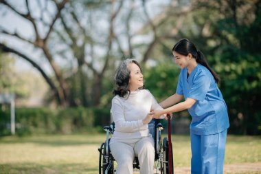 Asyalı genç bakıcı hemşire yaşlı bir erkeğin dışarıda yürümesini destekliyor. Uzman doktorlar yaşlı yetişkinlere yardım eder ve onlarla ilgilenir. Huzurevi hastane bahçesi konsepti