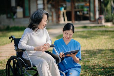Asyalı genç bakıcı hemşire yaşlı bir erkeğin dışarıda yürümesini destekliyor. Uzman doktorlar yaşlı yetişkinlere yardım eder ve onlarla ilgilenir. Huzurevi hastane bahçesi konsepti.