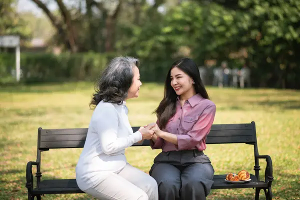 Mutlu yetişkin torun ve yaşlı büyükanne eğleniyor. Bahçede yeşil doğayla iç içe oturuyorlar.. 