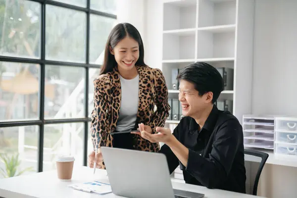 Asian business colleague business presents and explains and using laptop and tablet. Teamwork, financial marketing team,   while sitting in office room