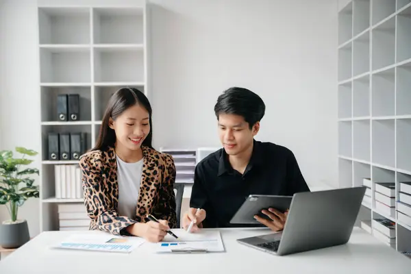Asian business colleague business presents and explains and using laptop and tablet. Teamwork, financial marketing team,   while sitting in office room