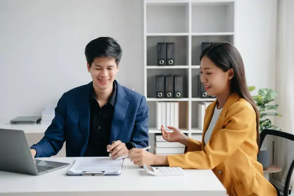 Asian business colleague business presents and explains and using laptop and tablet. Teamwork, financial marketing team,   while sitting in office room