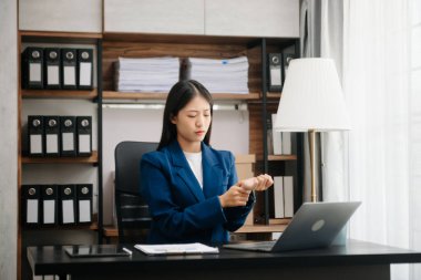 Asyalı kadın migren ağrısı çekiyor. Ofiste dizüstü bilgisayar ve tablet üzerinde çalışırken çok çalışan iş kadını finansör.