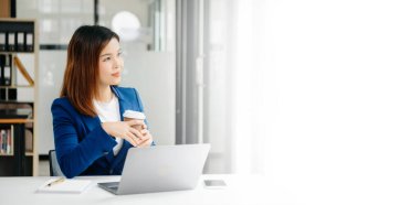 Kendine güvenen iş uzmanı, gülümseyen, dizüstü bilgisayarda yazan ve dijital tableti yaratıcı ofiste tutan çekici genç bir kadın..