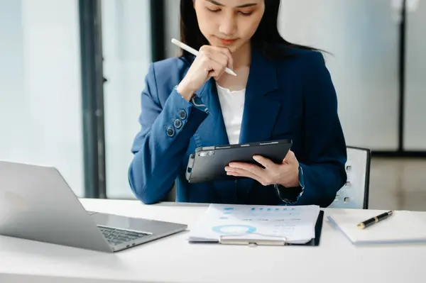 Tablet ve dizüstü bilgisayarda yazan genç ve güzel bir kadın beyaz masa modern ofisinde otururken.