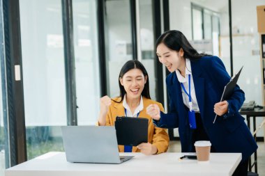 Asyalı iş arkadaşları sunar ve açıklar ve dizüstü bilgisayar ve tablet kullanır. Takım çalışması, finansal pazarlama ekibi, modern ofis odasında otururken.
