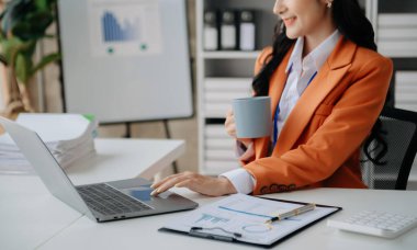 Laptop kullanan, dizüstü bilgisayarda yazan ve kahve fincanı tutan bir kadın.