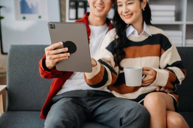 İki Asyalı öğrenci, bir dizüstü bilgisayar, tablet ve öğretmenle birlikte oturma odasında öğreniyor.