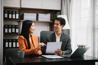 Asian business colleague business presents and explains and using laptop and tablet. Teamwork, financial marketing team,   while sitting in office room
