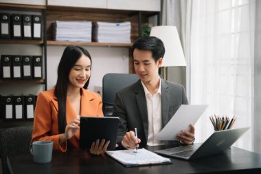 Asian business colleague business presents and explains and using laptop and tablet. Teamwork, financial marketing team,   while sitting in office room