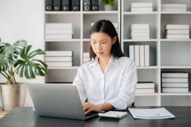 Confident Asian woman with a smile standing holding notepad and tablet at the modern office