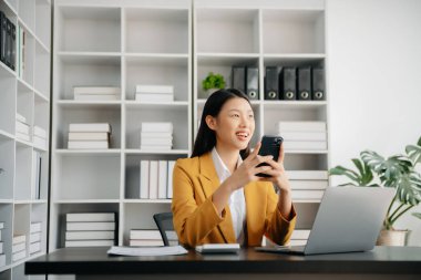 Confident Asian woman with a smile standing holding notepad and tablet at the modern office