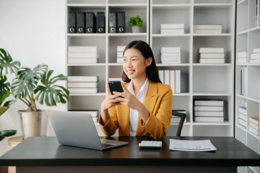 Confident Asian woman with a smile standing holding notepad and tablet at the modern office
