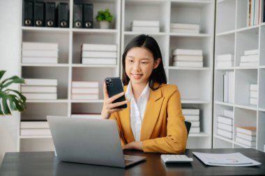 Confident Asian woman with a smile standing holding notepad and tablet at the modern office