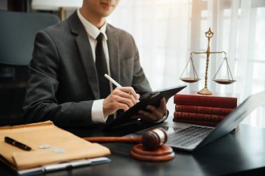 Adalet ve hukuk kavramı. Hukuk temalı ahşap masa, kitaplar, denge. Tokmak, mahkeme salonunda dijital tablet bilgisayarla çalışan bir erkek yargıç.
