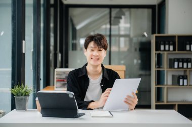 Modern ofiste elinde not defteri ve tabletle gülümseyen kendine güvenen Asyalı bir adam.