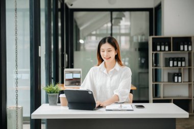 Tablet ve dizüstü bilgisayarda yazan genç ve güzel bir kadın beyaz çalışma masasında oturuyor.