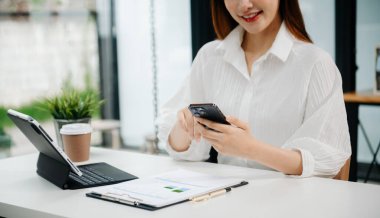 Ofiste bilgisayar, tablet ve akıllı telefon kullanan bir iş kadını. Dijital pazarlama medya mobil uygulaması ve yeni bir başlangıç projesi hakkında tartışmalar. Finans görevi