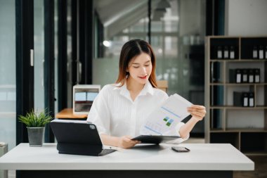 Tablet ve dizüstü bilgisayarda yazan genç ve güzel bir kadın beyaz çalışma masasında oturuyor.