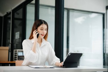 Tablet ve dizüstü bilgisayarda yazan genç ve güzel bir kadın beyaz çalışma masasında oturuyor.