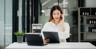 Tablet ve dizüstü bilgisayarda yazan genç ve güzel bir kadın beyaz çalışma masasında oturuyor.