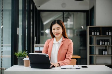 Tablet ve dizüstü bilgisayarda yazan genç ve güzel bir kadın beyaz çalışma masasında oturuyor.