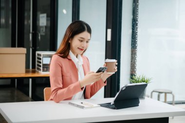 Tablet ve dizüstü bilgisayarda yazan genç ve güzel bir kadın beyaz çalışma masasında oturuyor.