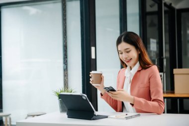 Çalışan not defteri, tablet ve laptop belgeleriyle modern ofiste çalışan Asyalı iş kadını.