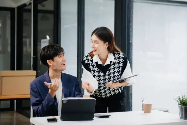 Asian business colleague business presents and explains and using laptop and tablet. Teamwork, financial marketing team,   while sitting in office room