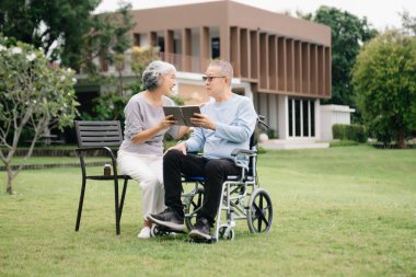 Tekerlekli sandalyede oturmuş birbirlerine göz kulak oluyorlar. Romantik bir zamanda parkta otururken gülüp gülüyorlar.