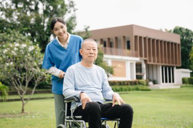 Asyalı yaşlı, yaşlı, yaşlı, tekerlekli sandalyede, Asyalı, dikkatli bir bakıcı ve bahçede yürüyen bir hastayı cesaretlendiren bir kadın. Bakıcının ve kıdemli sağlık sigortasının dikkatine.