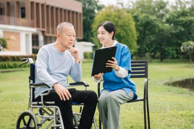 Asyalı dikkatli bakıcı ya da hemşire ve tekerlekli sandalyedeki mutlu hasta bahçede yürüyorlar. Yeşil doğayla zihninizi dinlendirmek ve cesaretlendirmek için. Dinlemek için steteskop kullan.