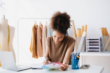 Sakin kıvırcık esmer, esmer kadın moda tasarımcısının ofisinde ve elinde tablet ve akıllı telefon var.