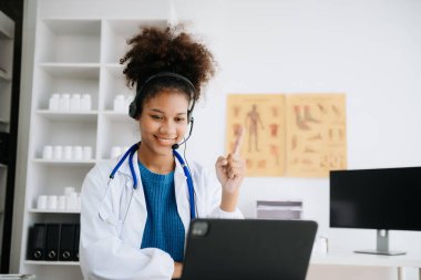 İş masasında oturan Afrikalı kadın doktor. İnternette tıbbi, sağlık konsepti. Doktor iş için dizüstü bilgisayar kullanıyor, iş arkadaşlarıyla görüntülü konuşma yapıyor.