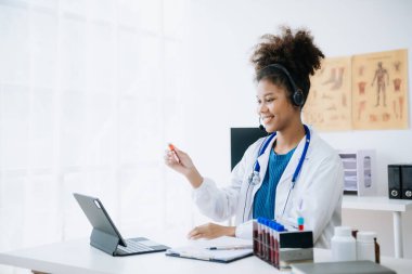 İş masasında oturan Afrikalı kadın doktor. İnternette tıbbi, sağlık konsepti. Doktor iş için dizüstü bilgisayar kullanıyor, iş arkadaşlarıyla görüntülü konuşma yapıyor.