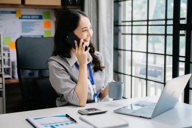 Kendine güvenen iş uzmanı çekici, gülümseyen genç bir kadın. Ofiste elinde dijital tabletle dizüstü bilgisayarı yazıyor..