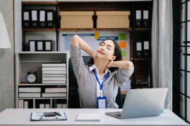 Asyalı kadın migren ağrısı çekiyor. Ofiste dizüstü bilgisayar ve tablet üzerinde çalışırken çok çalışan iş kadını finansör.