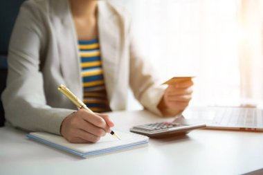 İş kadını, internet üzerinden alışveriş yapmak için kredi kartıyla hesap makinesi ve ofis içi finans stratejisi kullanıyor.