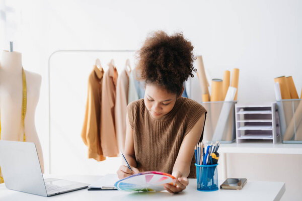 Спокойная курчавая брюнетка темнокожая женщина в офисе модельера и держит планшет и смартфон